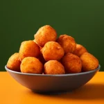 A bowl of hushpuppies on a table against a dark green wall for the blog post titled, "How to make light and fluffy hushpuppies."