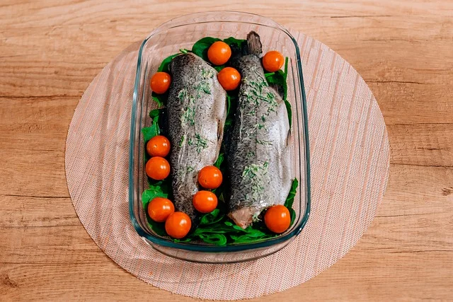 Two whole trouts with cherry tomatoes and leafy greens in a glass baking dish. 